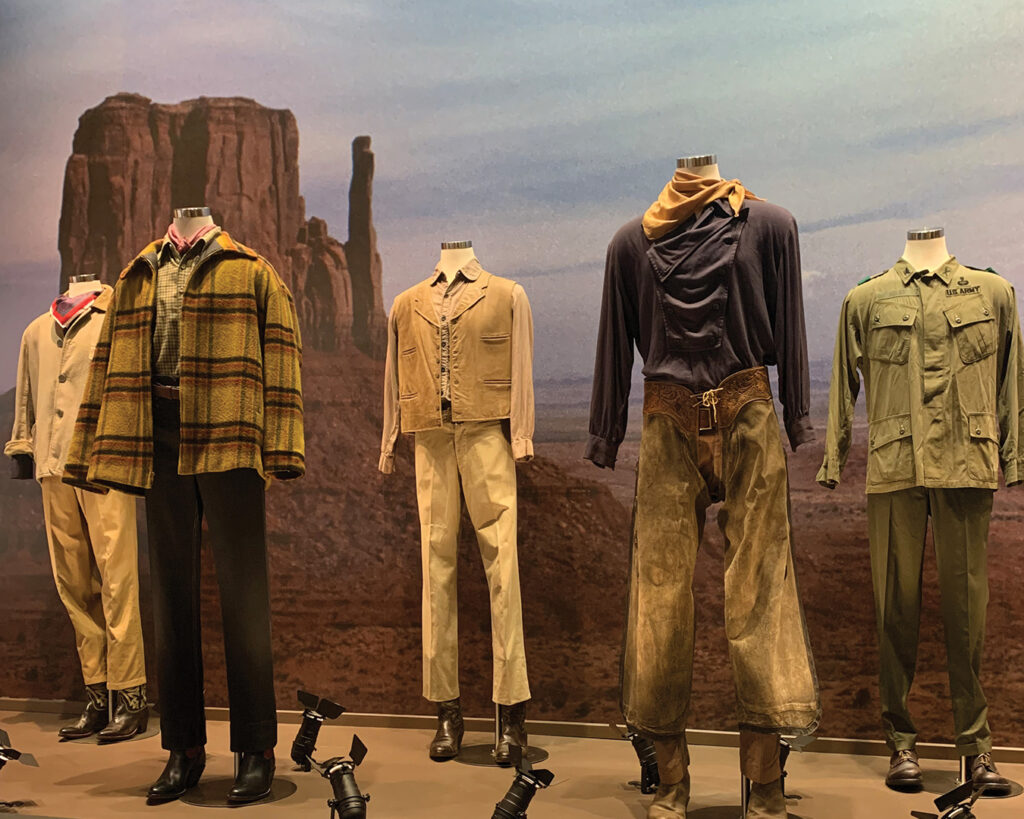 The Cowboys costume ensemble worn by John Wayne in the 1972 film, featuring vest, mauve shirt, and khaki pants, displayed at John Wayne: An American Experience.
Caption: John Wayne’s screen-worn costume from The Cowboys (1972).