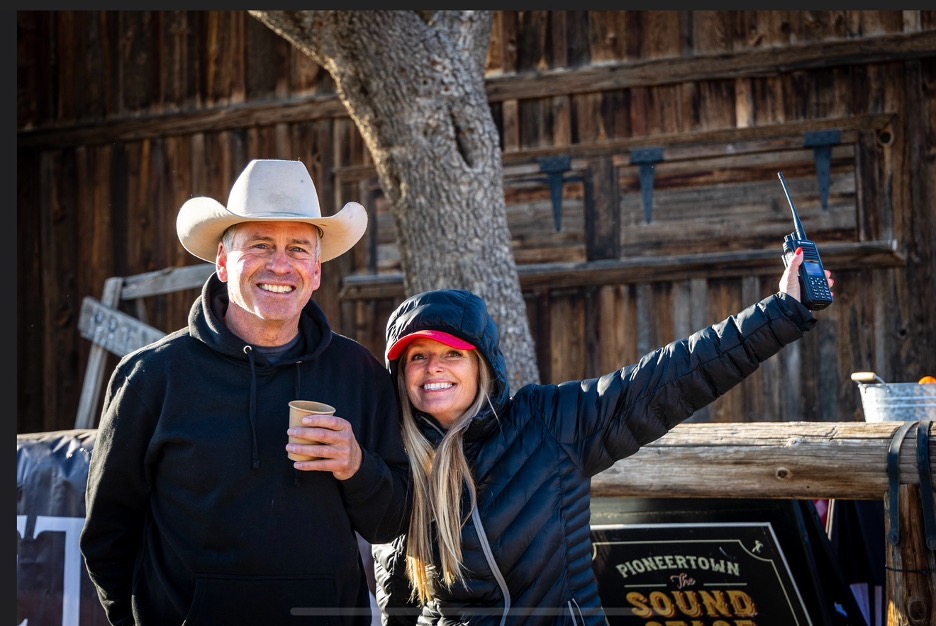 Race Director Molly Kassouf stands with Ethan Wayne, President of John Wayne Enterprises, during a Grit Series event in Fort Worth. Both smile as they celebrate the spirit of grit and community that defines the John Wayne Cancer Foundation.